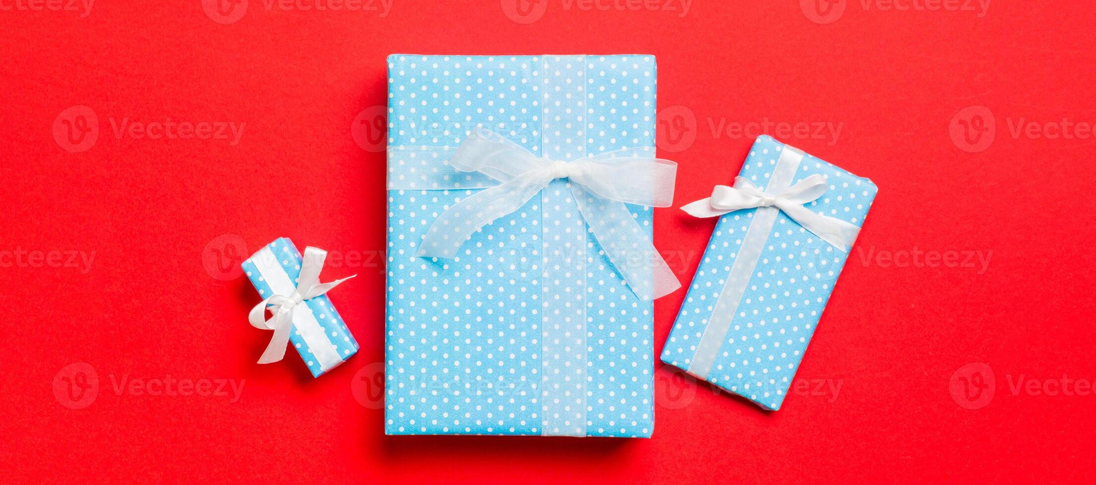 wrapped Christmas or other holiday handmade present in paper with white ribbon on red background. Present box, decoration of gift on colored table, top view photo