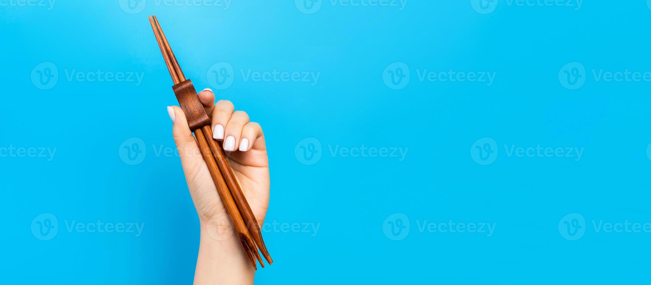 imagen recortada de la mano femenina sosteniendo palillos sobre fondo azul. concepto de comida japonesa con espacio de copia foto