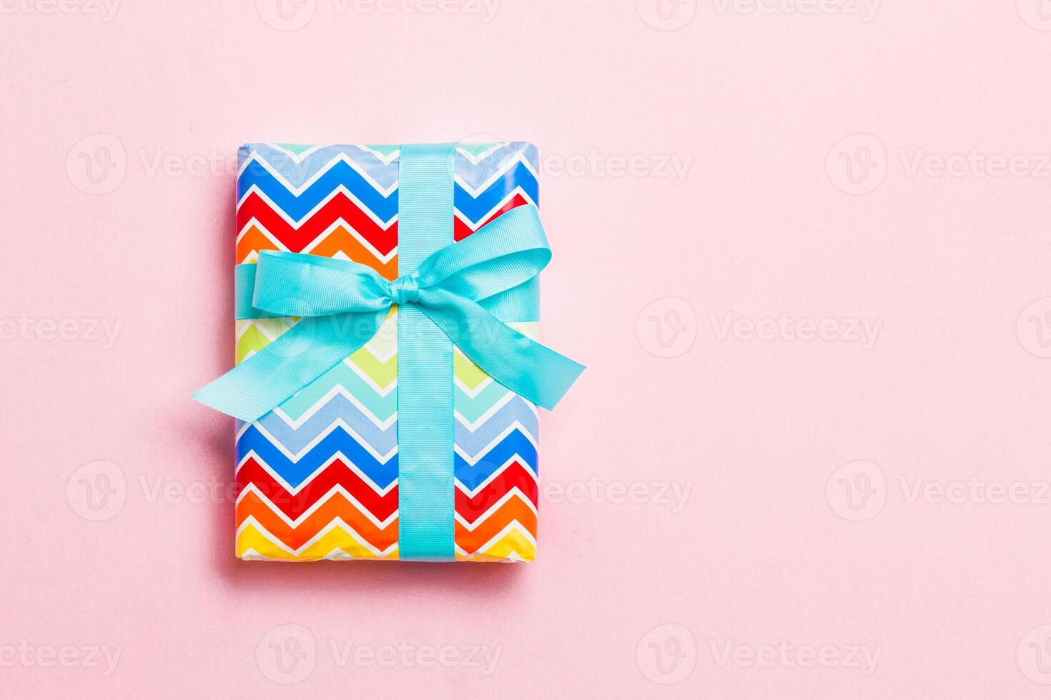 wrapped Christmas or other holiday handmade present in paper with blue ribbon on pink background. Present box, decoration of gift on colored table, top view with copy space photo