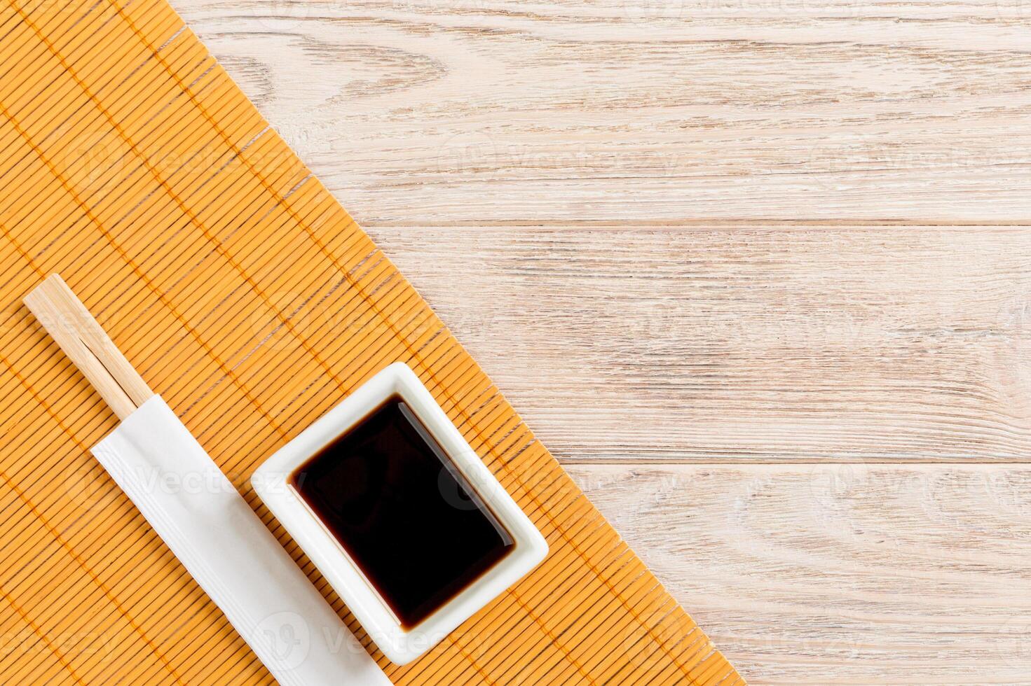 Bamboo mat and soy sauce with sushi chopsticks on wooden table. Top view with copy space background for sushi. Flat lay photo