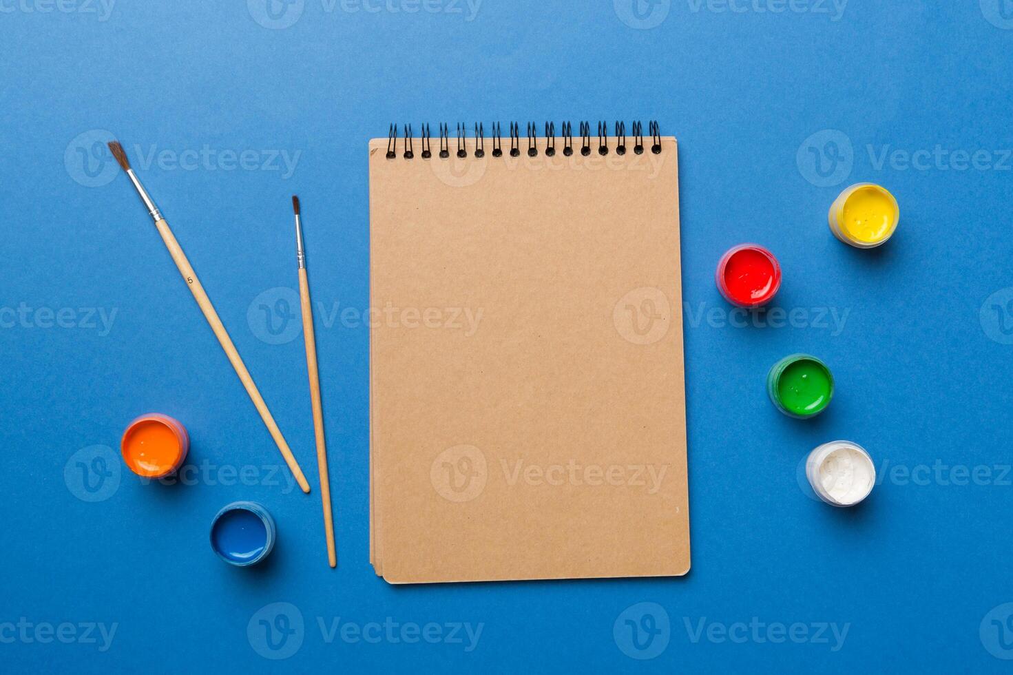 Album pages and paints, pencils, brush on a colored background. Top view with empty space. workplace for creativity. home teaching concept drawing photo