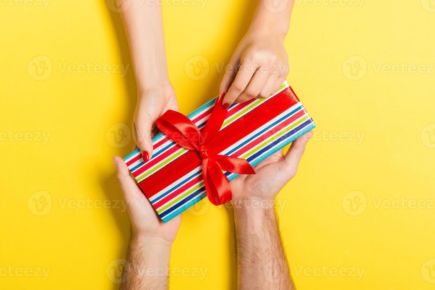 Top view of giving and receiving a gift on colorful background. Present in male and female hands. Love concept. Close up photo