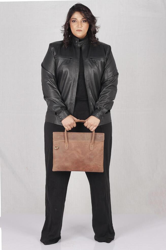 un mujer en un negro cuero chaqueta y negro pantalones con marrón cuero mano bolso foto