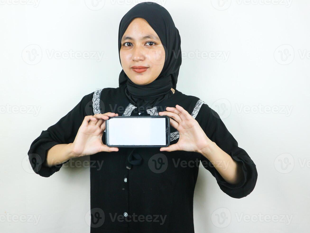 Young Muslim woman in hijab smiling showing mobile phone blank screen recommending App photo