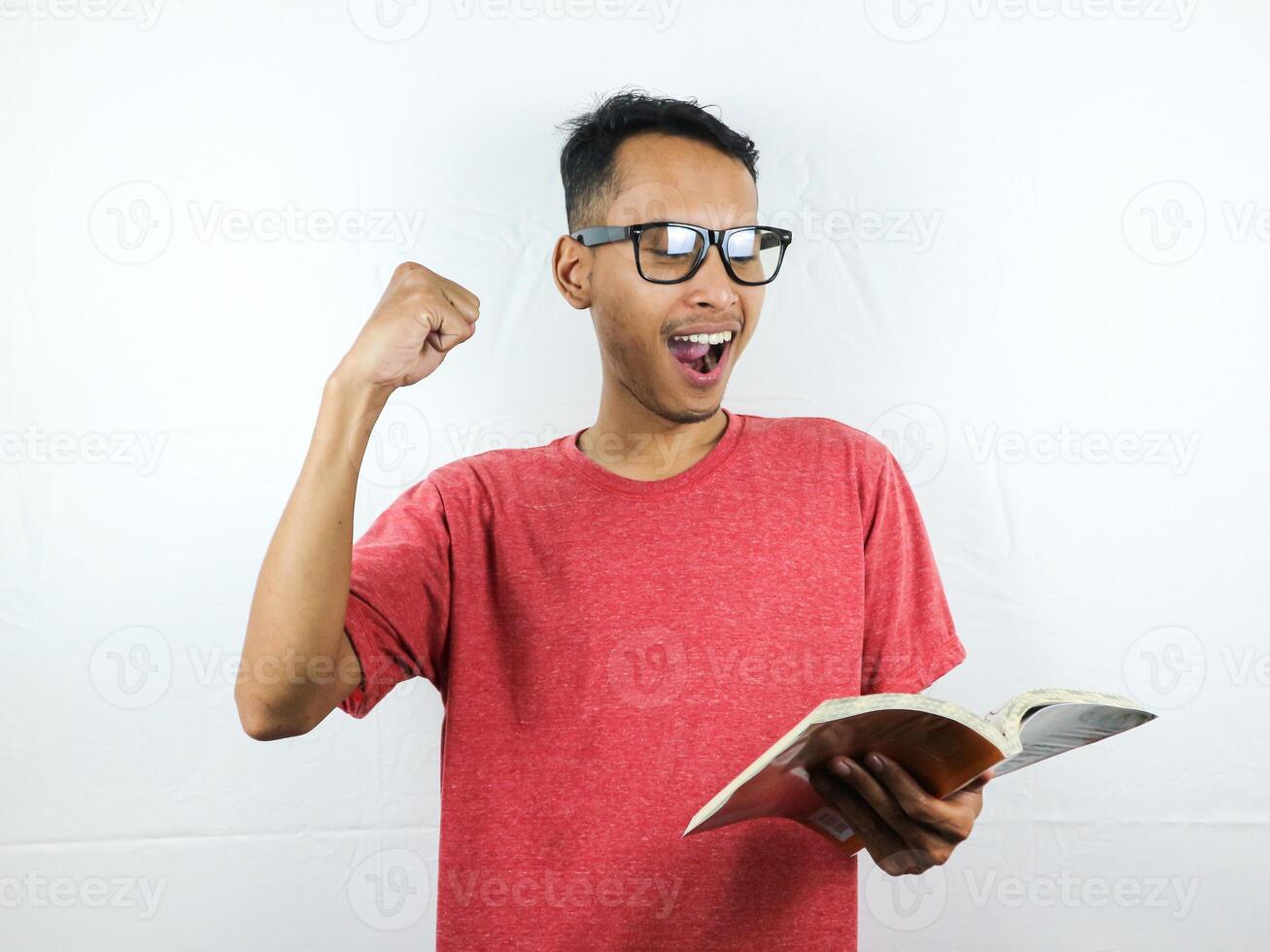 portrait of smiling asian man holding and reading book while clenching fist. photo