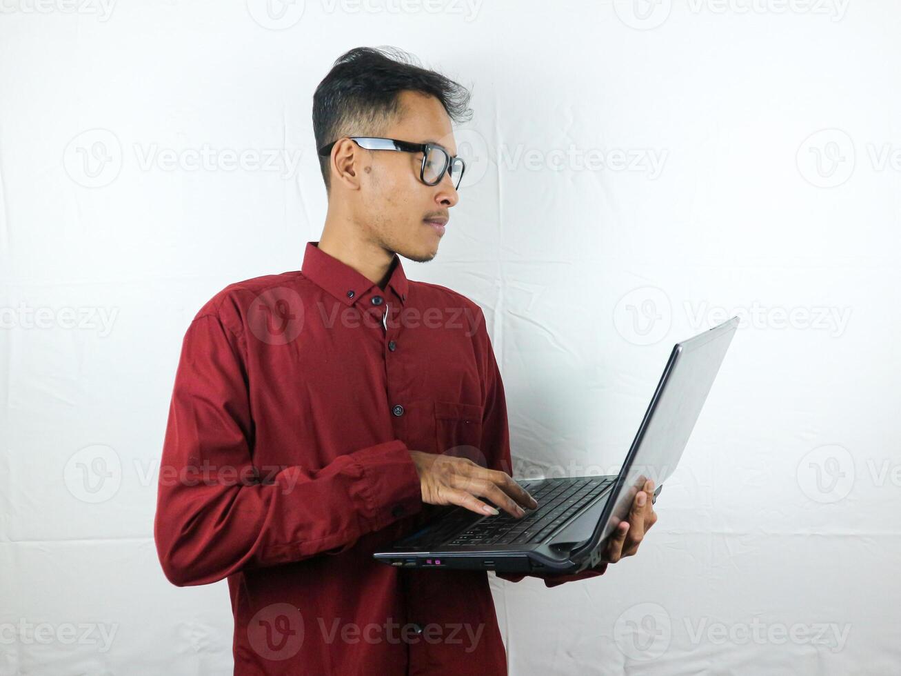 portrait of asian man holding laptop and typing with focused expression. advertising concept. photo