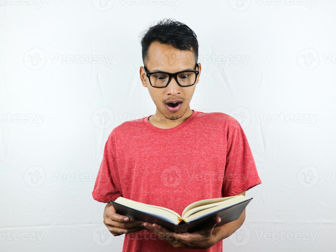 retrato de un asiático hombre con un conmocionado expresión mientras leyendo un libro. foto