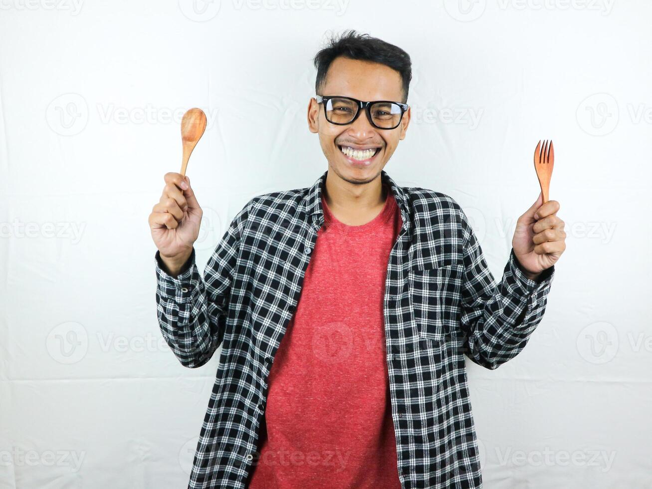 emocionado asiático hombre participación cuchara y tenedor en su manos foto