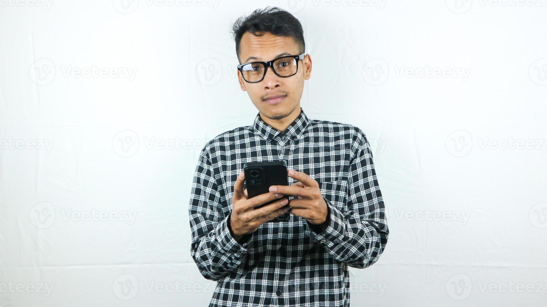 Portrait of asian man holding mobile phone reading, typing message while looking at camera. photo