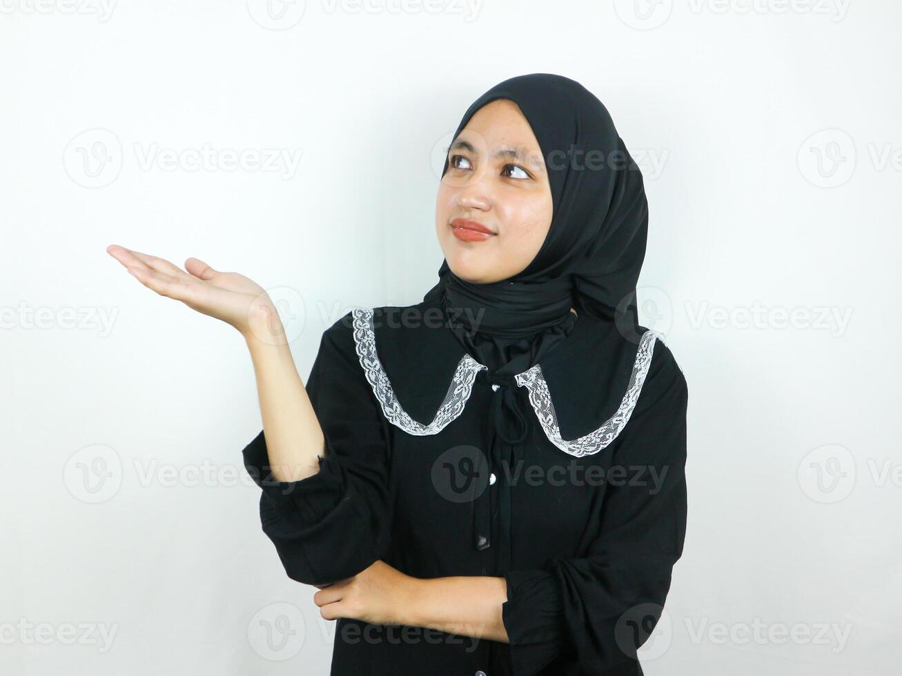 Cheerful beautiful Asian Muslim woman in hijab presenting copy space on palm, Advertising concept photo