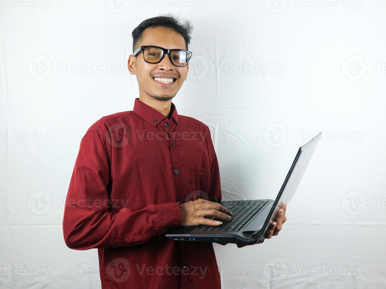 portrait of an asian man wearing a red clothes holding a laptop with a smiling face expression. photo