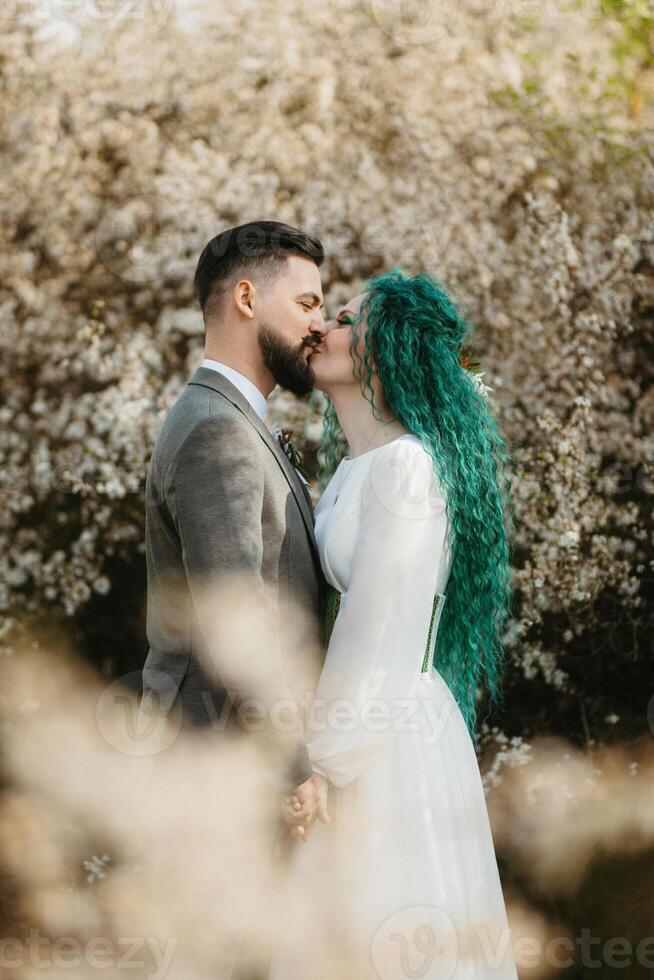 a bearded groom plays and a girl with green hair against the background of blooming spring photo