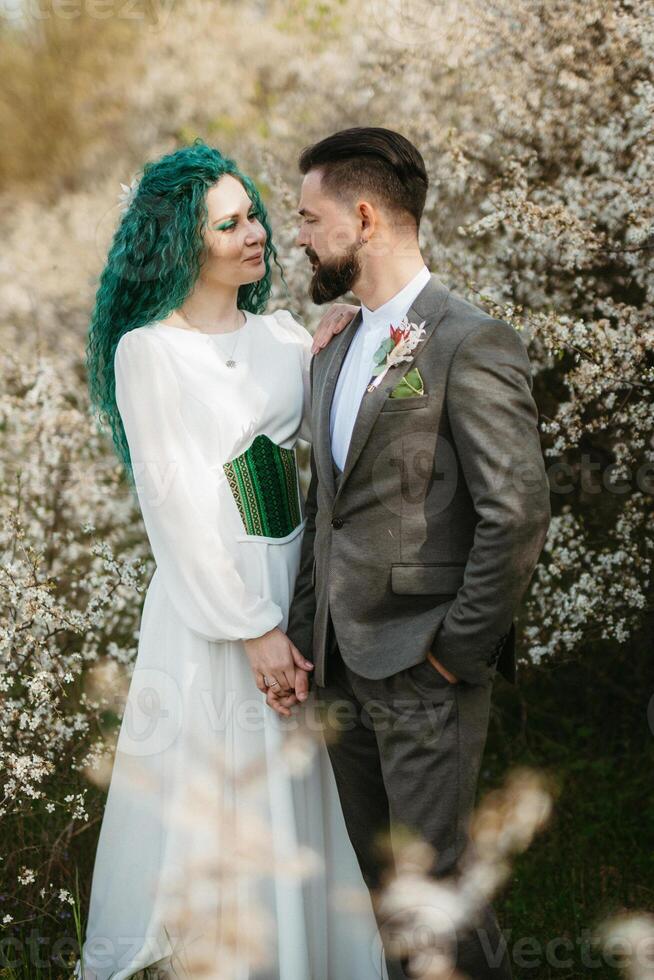 a bearded groom plays and a girl with green hair against the background of blooming spring photo