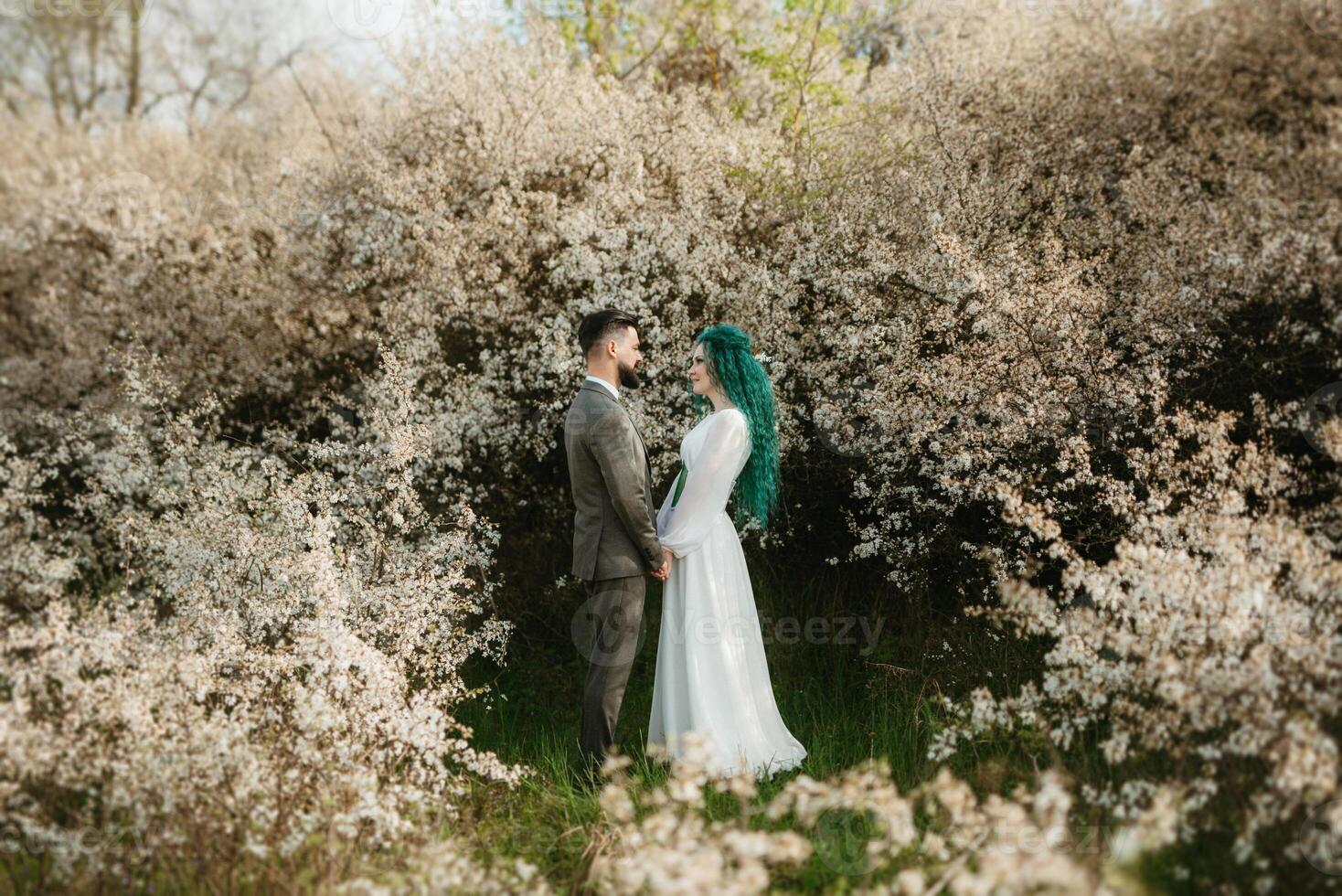 a bearded groom plays and a girl with green hair against the background of blooming spring photo