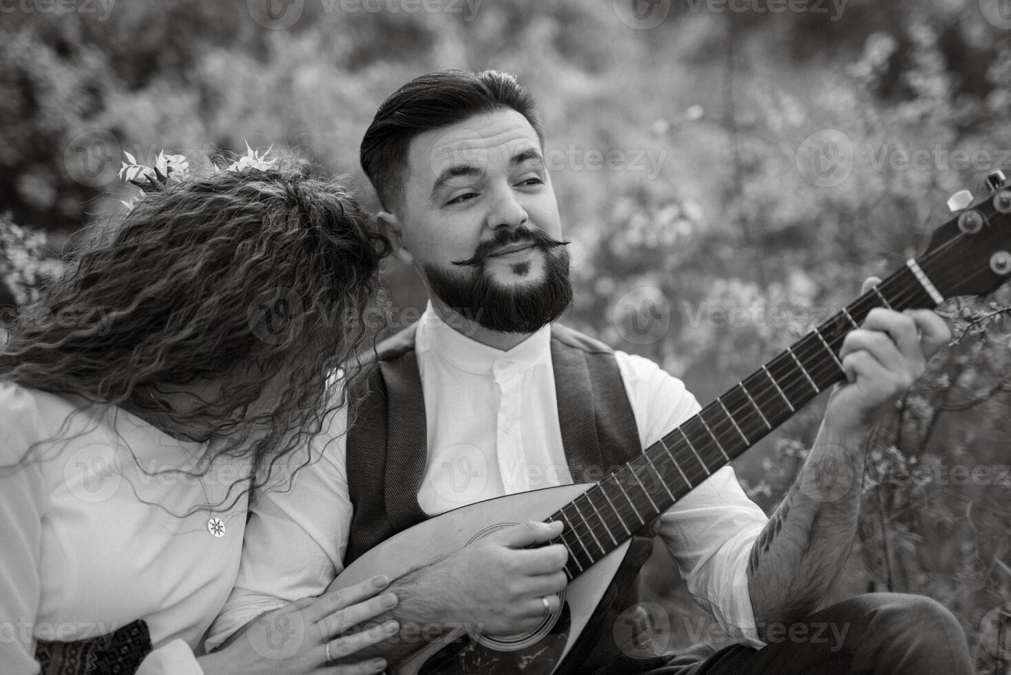 a bearded groom plays a stringed instrument and a girl sits in a spring meadow photo