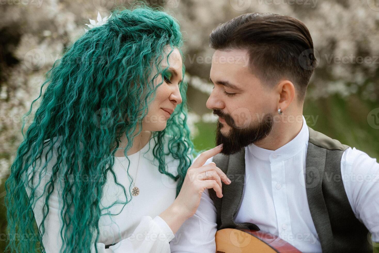 a bearded groom plays a stringed instrument and a girl with sits in a spring meadow photo