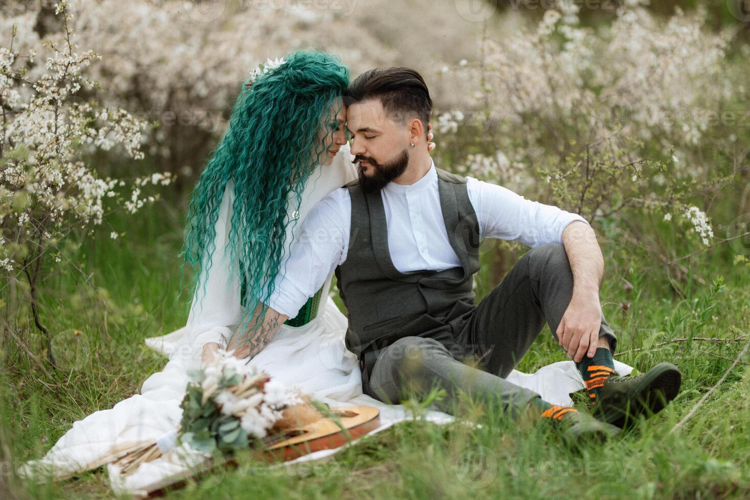 a bearded groom plays a stringed instrument and a girl sits in a spring meadow photo