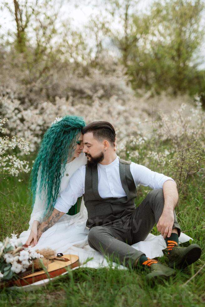 a bearded groom plays a stringed instrument and a girl sits in a spring meadow photo