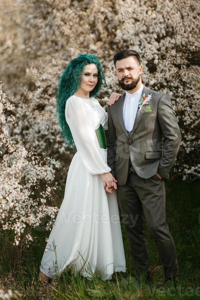 a bearded groom plays and a girl with green hair against the background of blooming spring photo