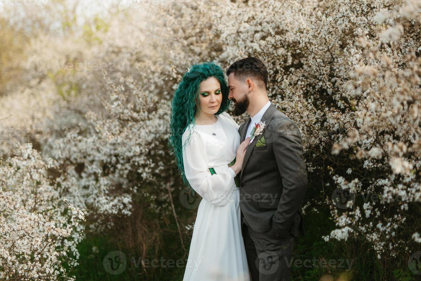a bearded groom plays and a girl with green hair against the background of blooming spring photo