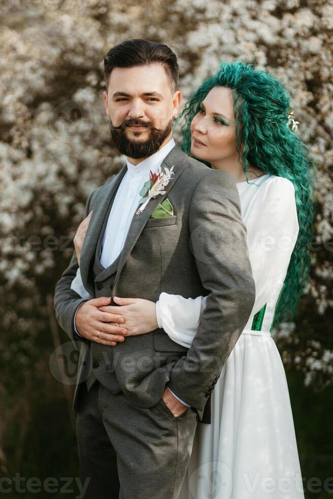 a bearded groom plays and a girl with green hair against the background of blooming spring photo