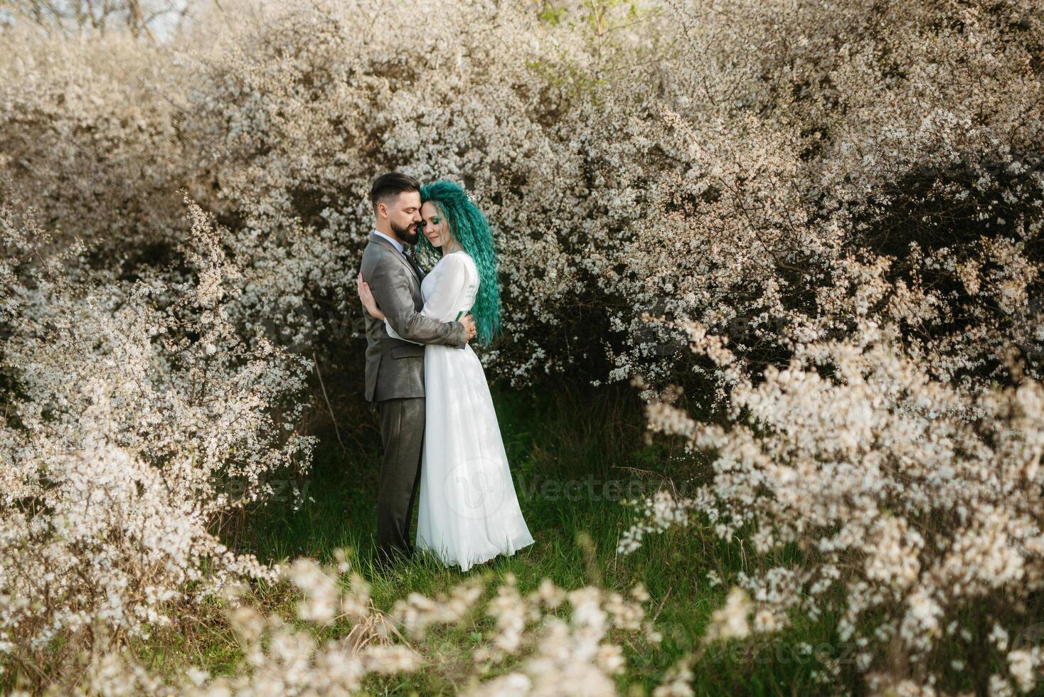 a bearded groom plays and a girl with green hair against the background of blooming spring photo