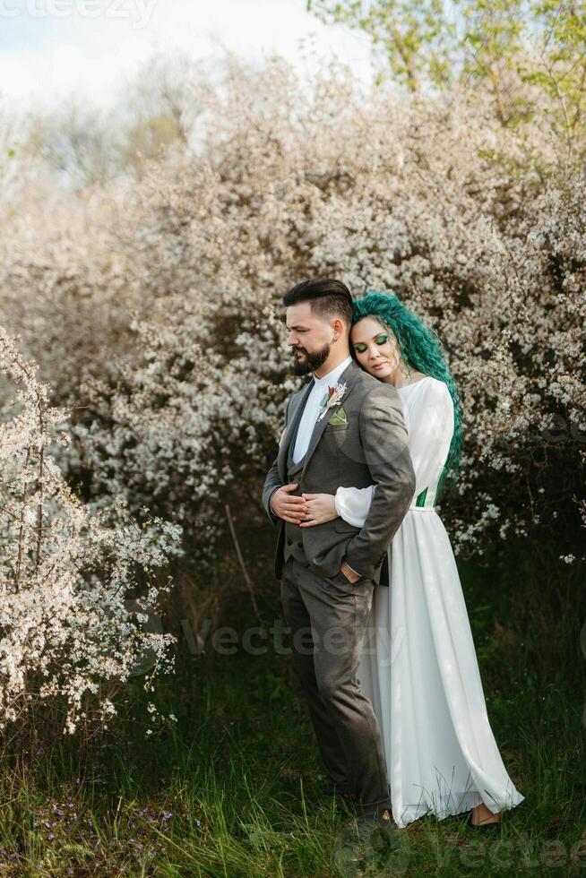 a bearded groom plays and a girl with green hair against the background of blooming spring photo