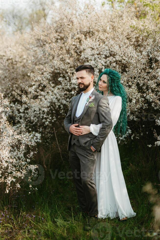 a bearded groom plays and a girl with green hair against the background of blooming spring photo