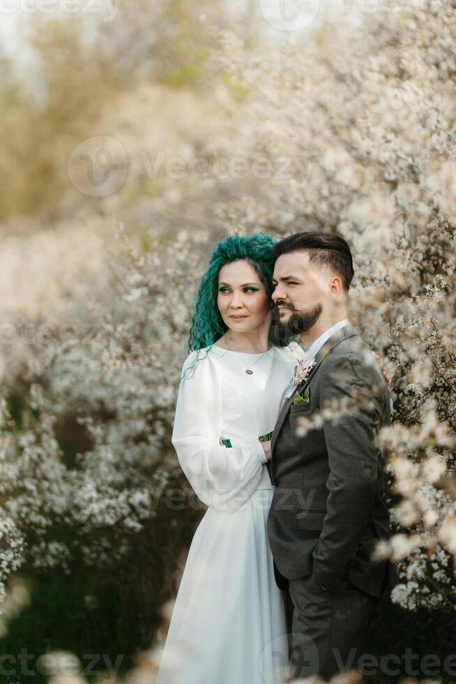 a bearded groom plays and a girl with green hair against the background of blooming spring photo