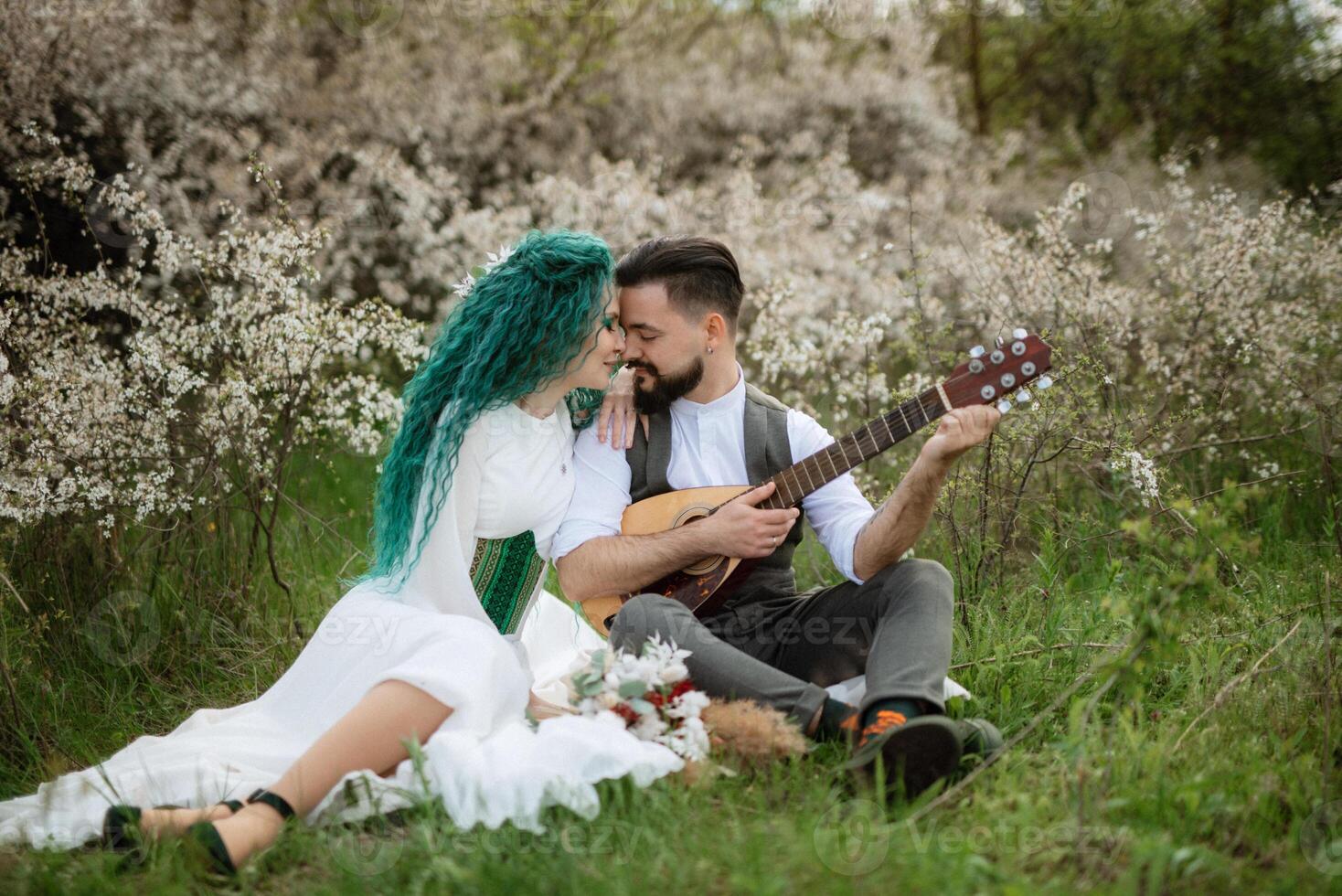 a bearded groom plays a stringed instrument and a girl sits in a spring meadow photo