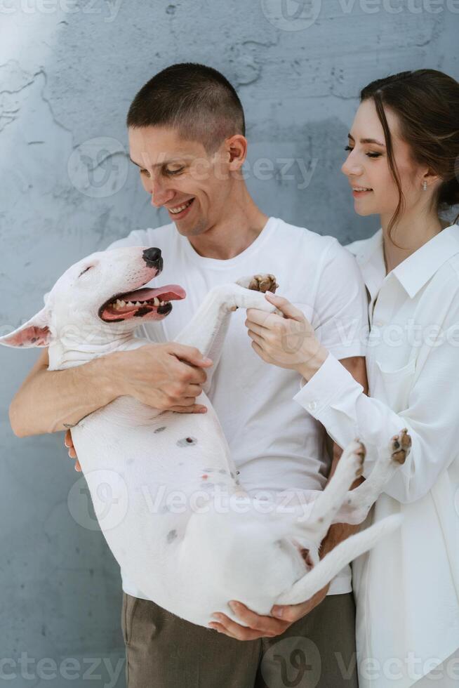 young couple guy and girl in a bright room playing with pet photo