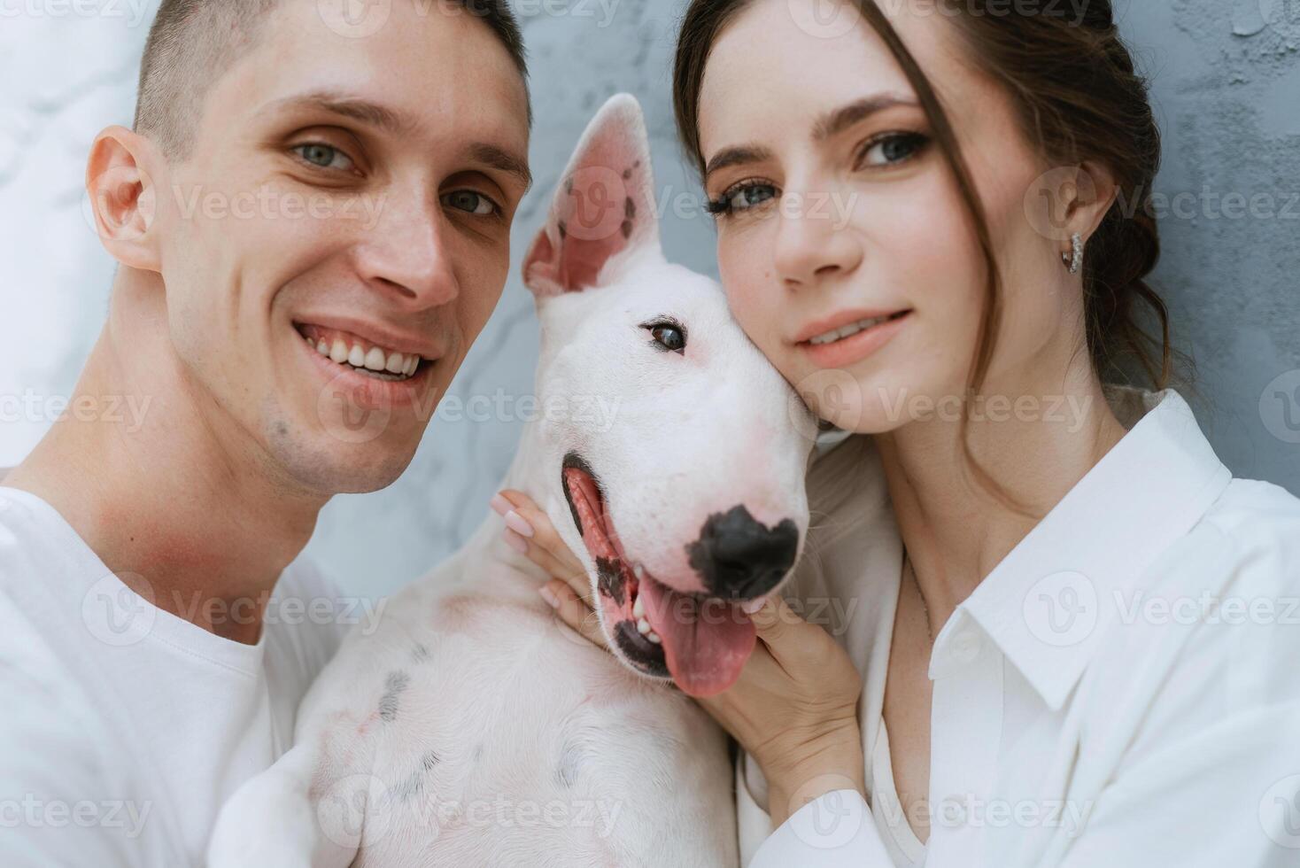 young couple guy and girl in a bright room playing with pet photo