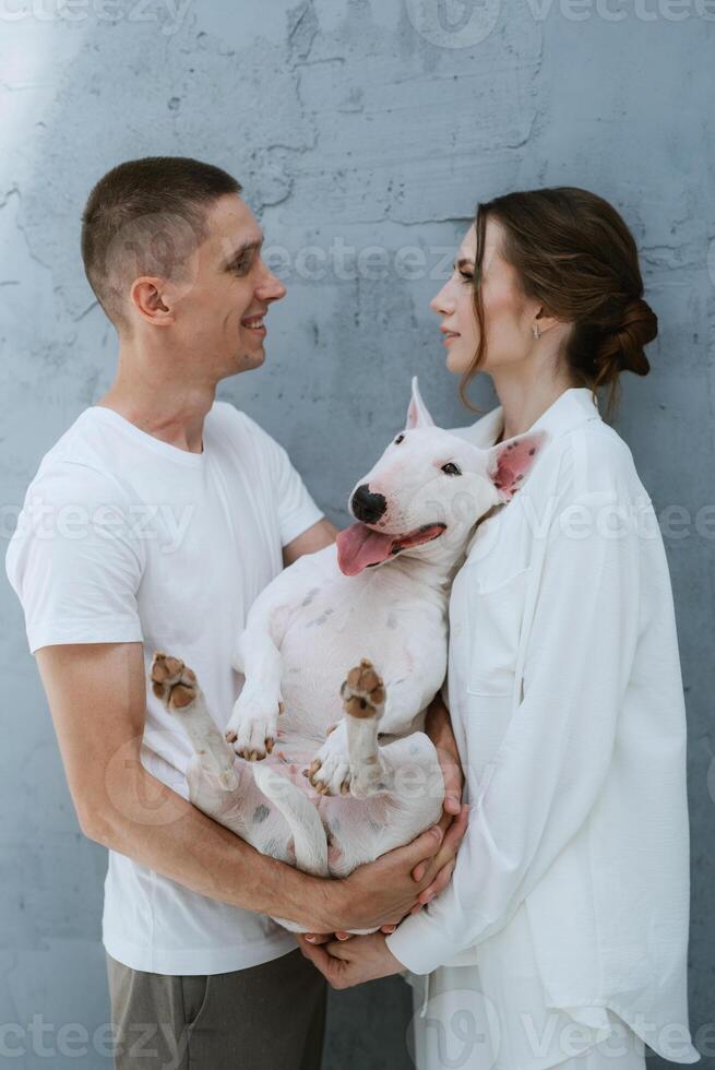 young couple guy and girl in a bright room playing with pet photo