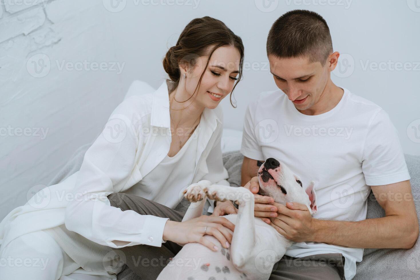young couple guy and girl in a bright room playing with pet photo