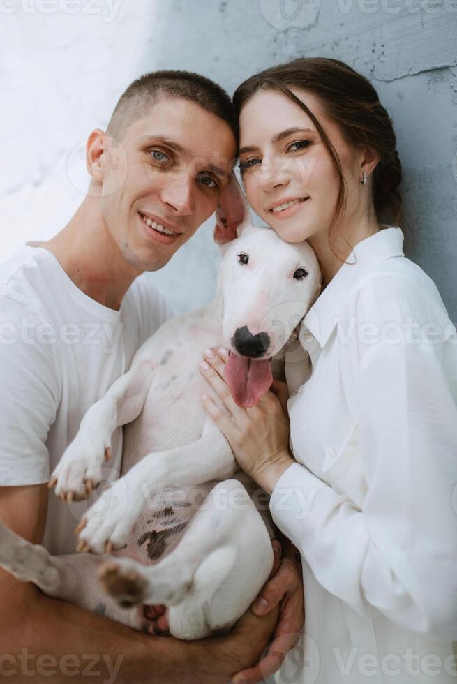 young couple guy and girl in a bright room playing with pet photo