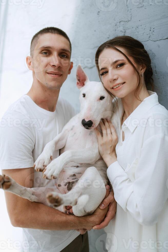 young couple guy and girl in a bright room playing with pet photo