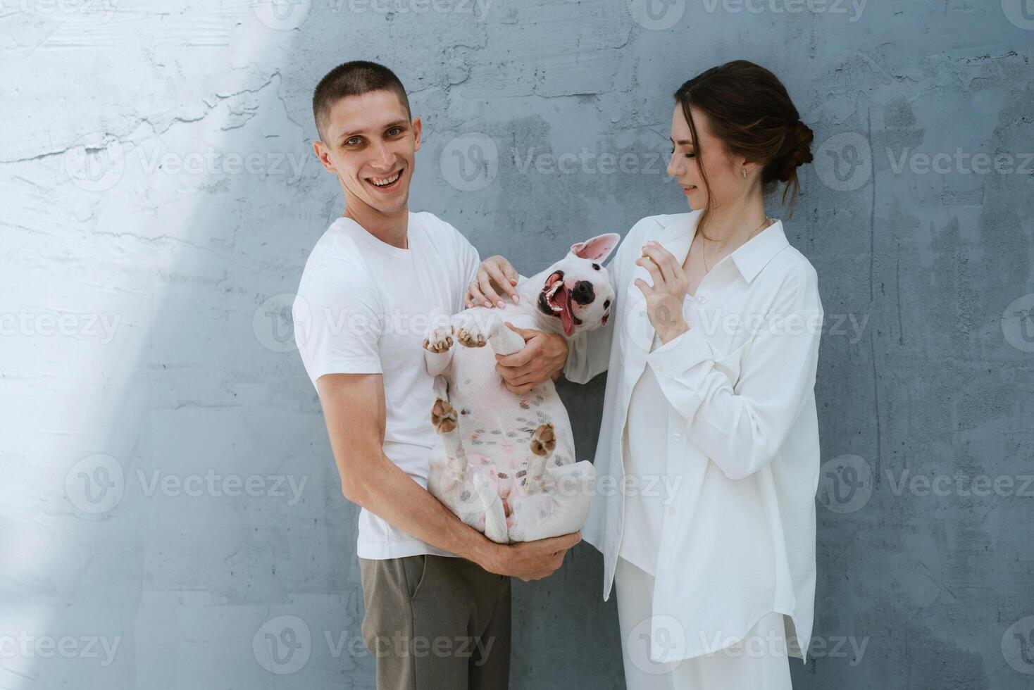young couple guy and girl in a bright room playing with pet photo