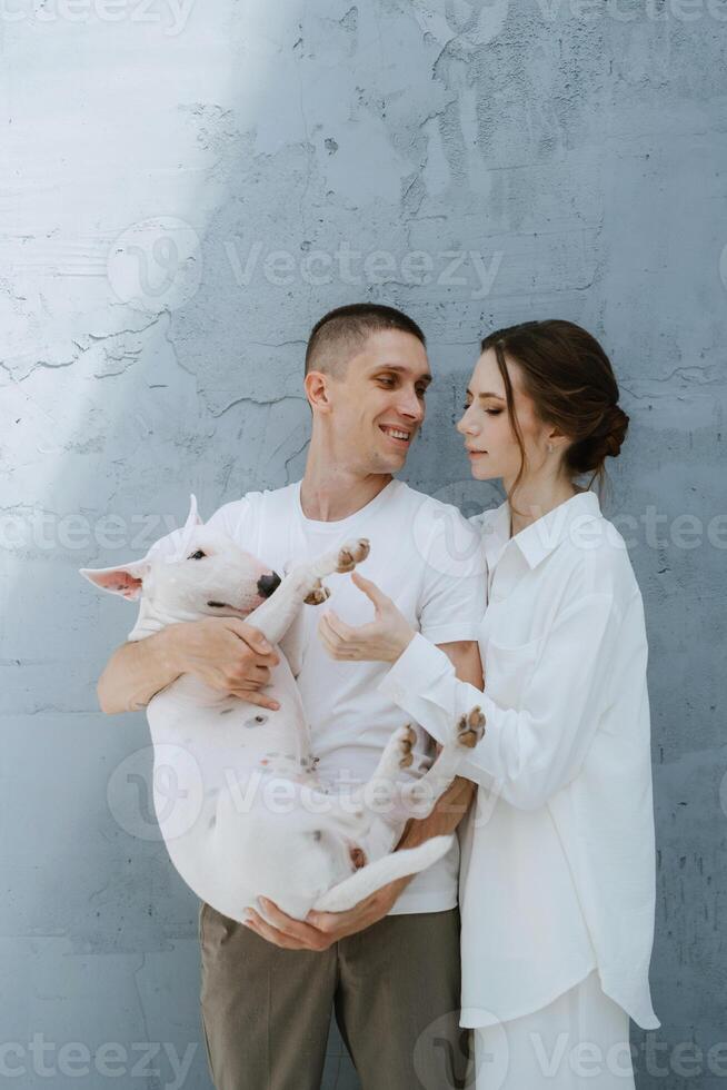 young couple guy and girl in a bright room playing with pet photo