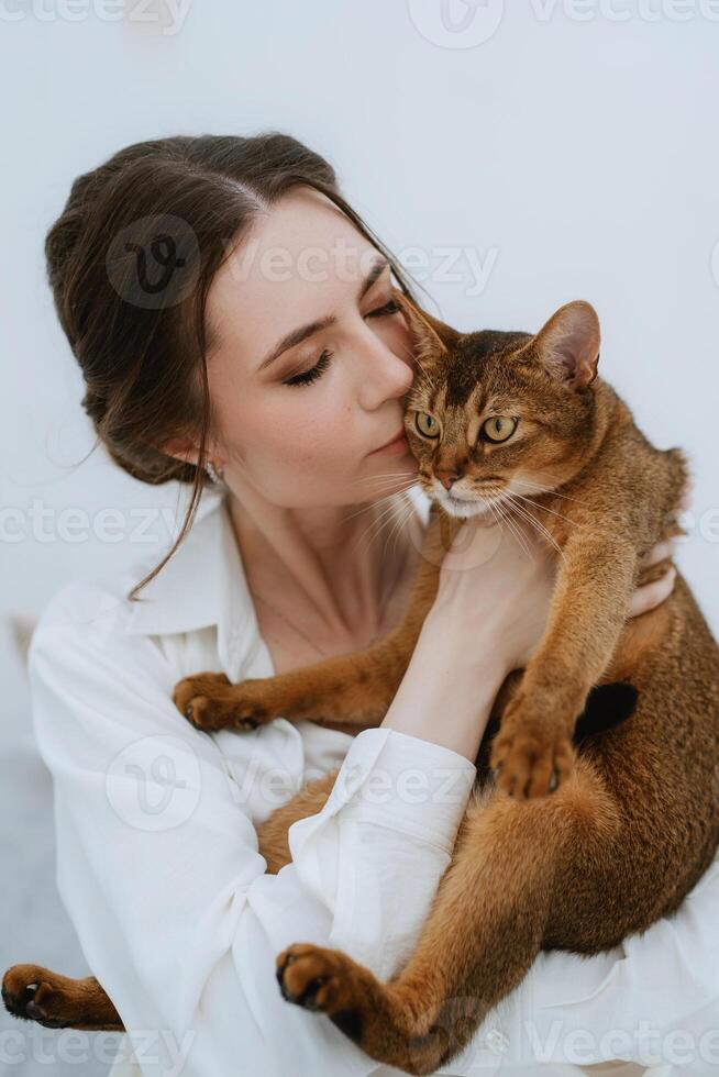 joven niña en un blanco habitación jugando con un gato foto