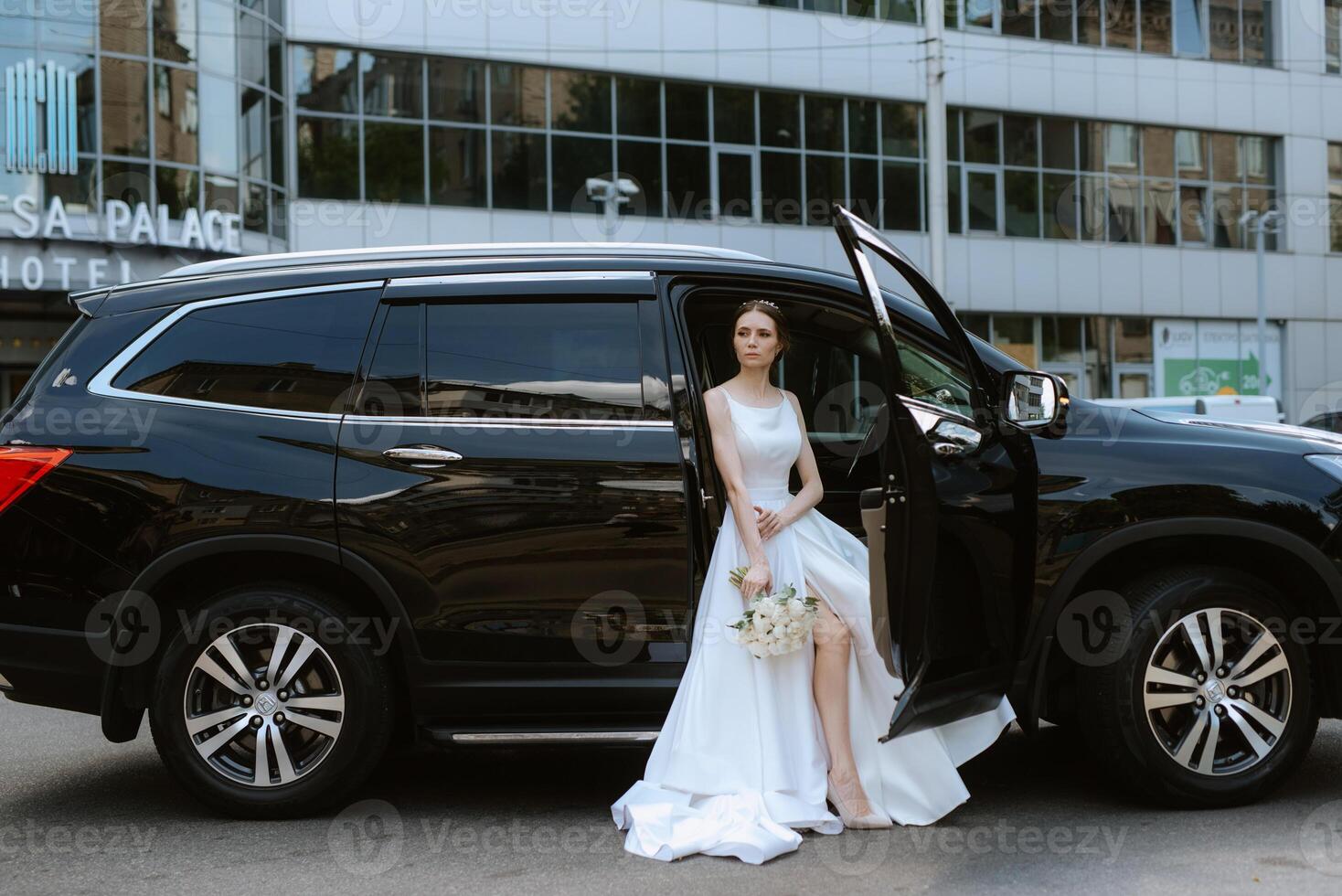 bride with a black car near a glass skyscraper photo