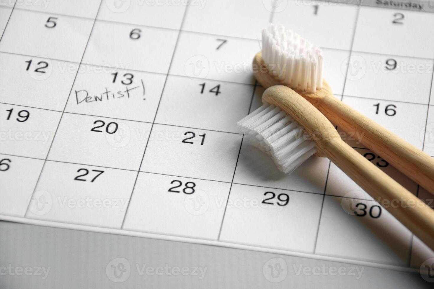 On a light gray background, there is a calendar with a dentist's note and toothbrushes. photo