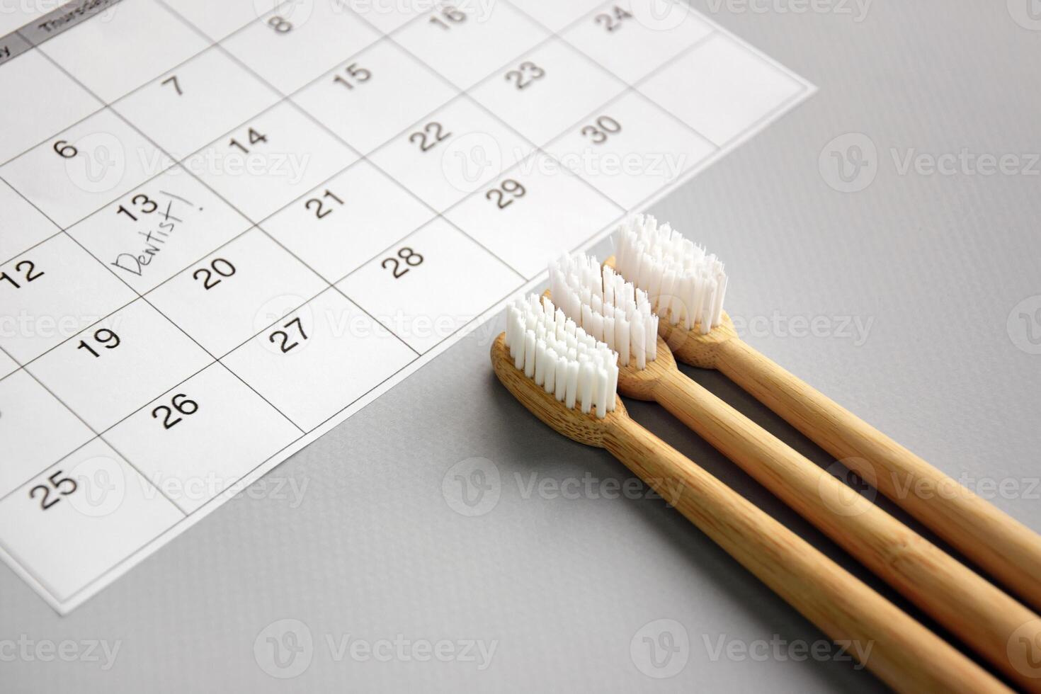 On a light gray background, there is a calendar with a dentist's note and toothbrushes. photo