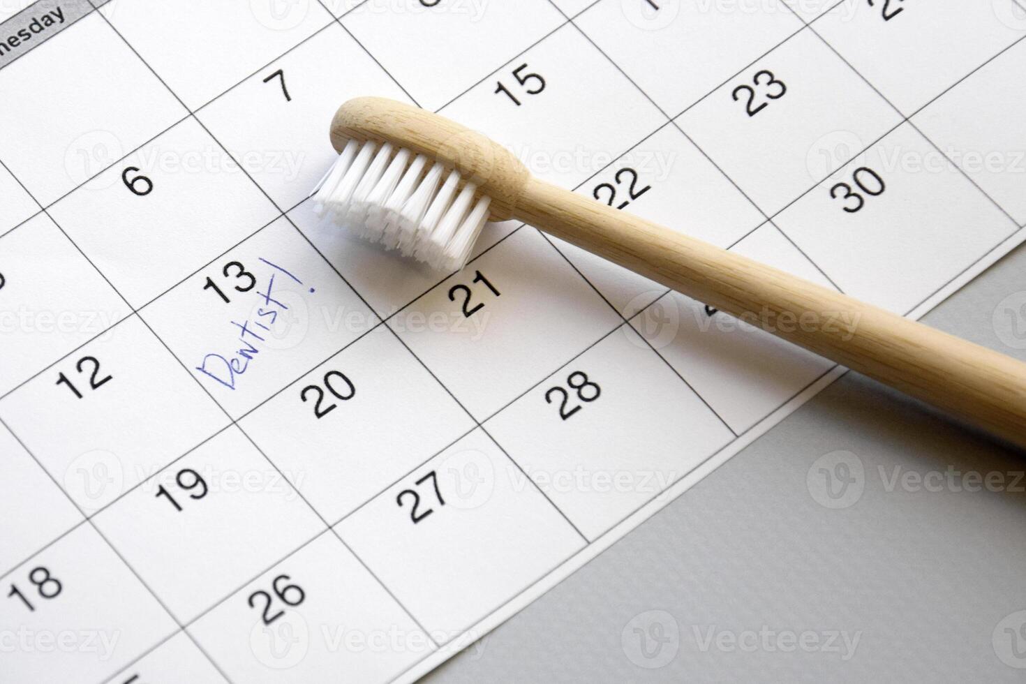 On a light gray background, there is a calendar with a dentist's note and toothbrushes. photo