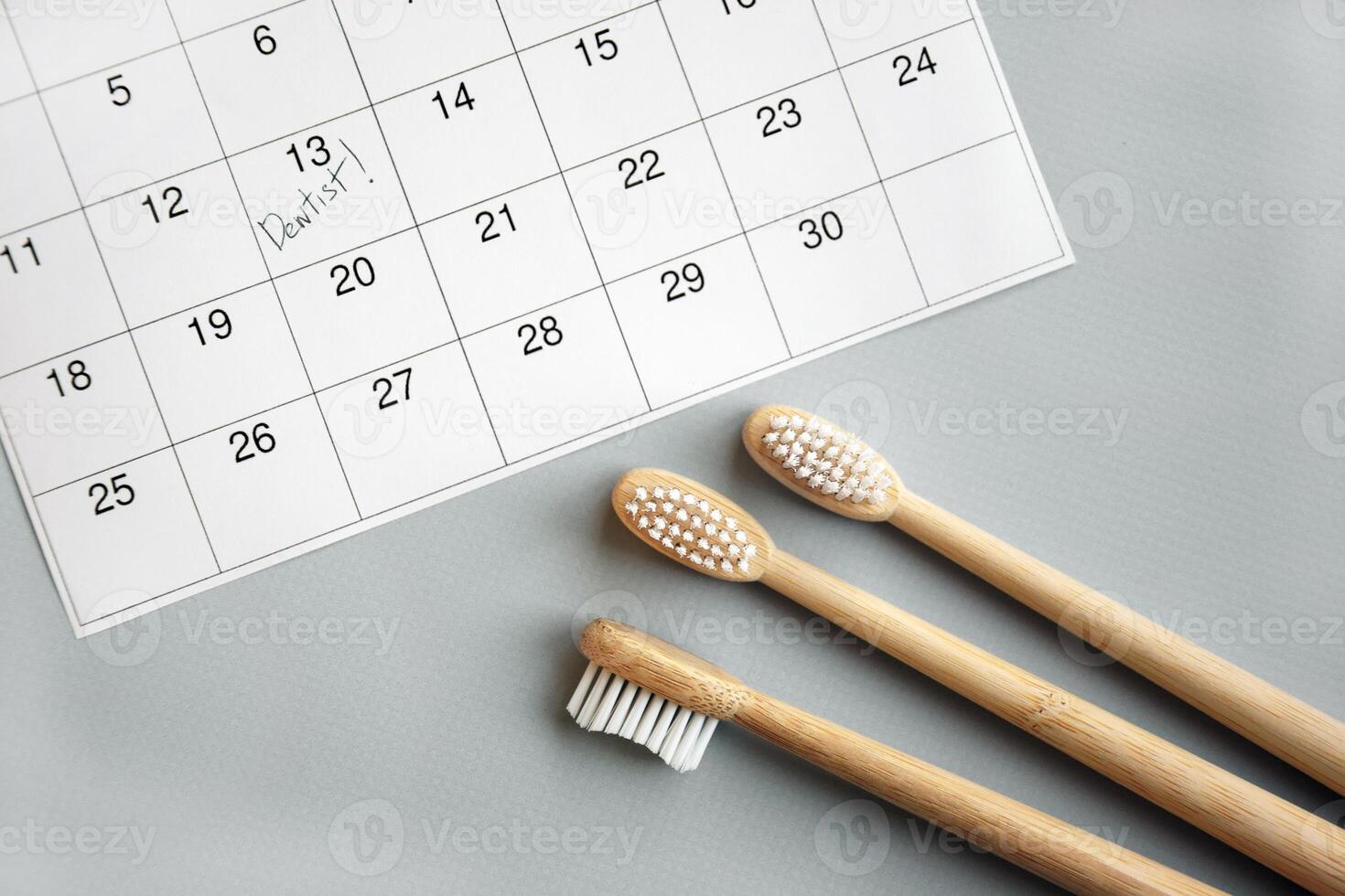 On a light gray background, there is a calendar with a dentist's note and toothbrushes. photo