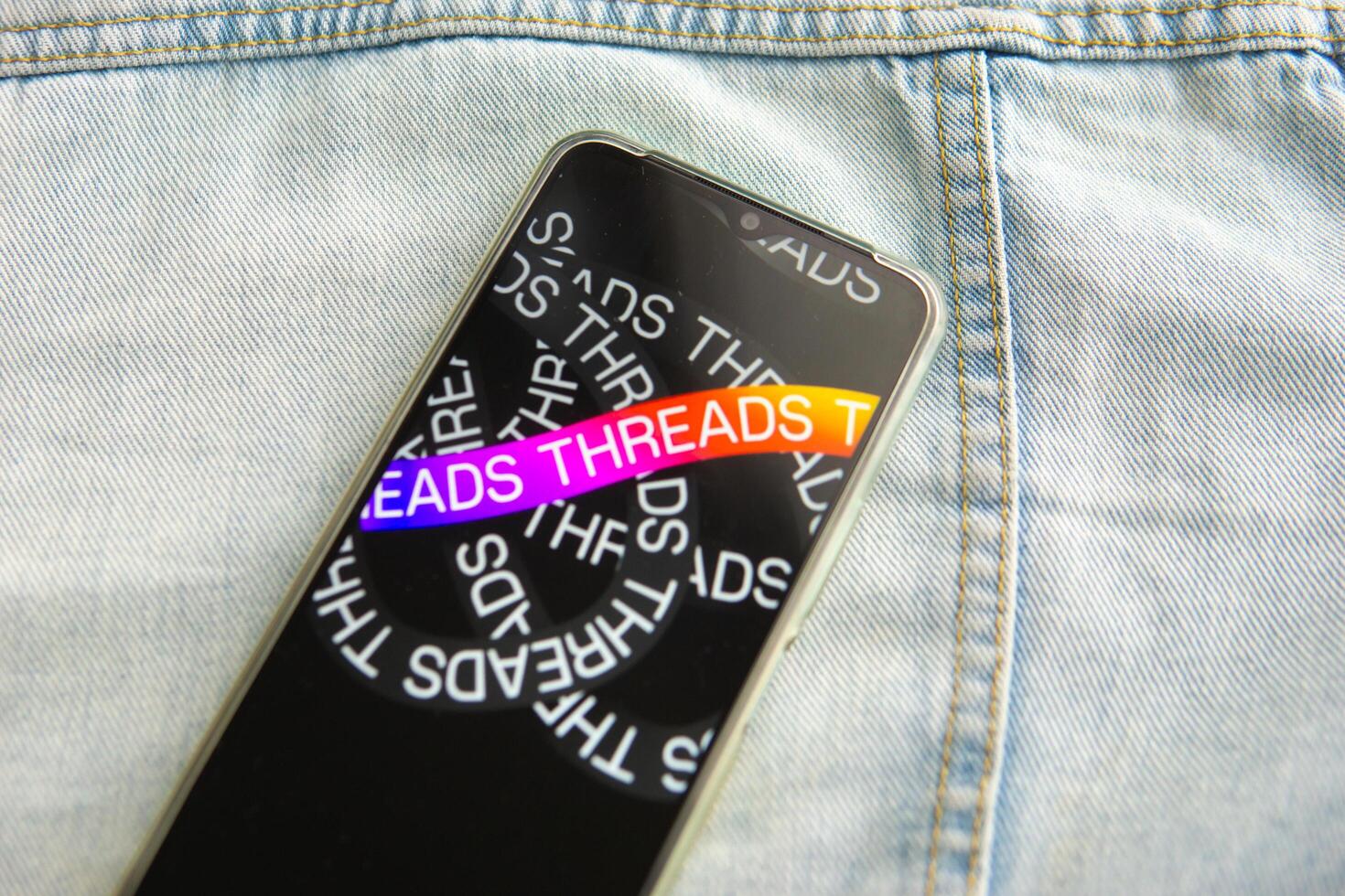 Tver, Russia - July 15, 2023, the threads logo on the smartphone screen lying on the jeans. The threads icon. The logo of the current application. Threads social network. photo