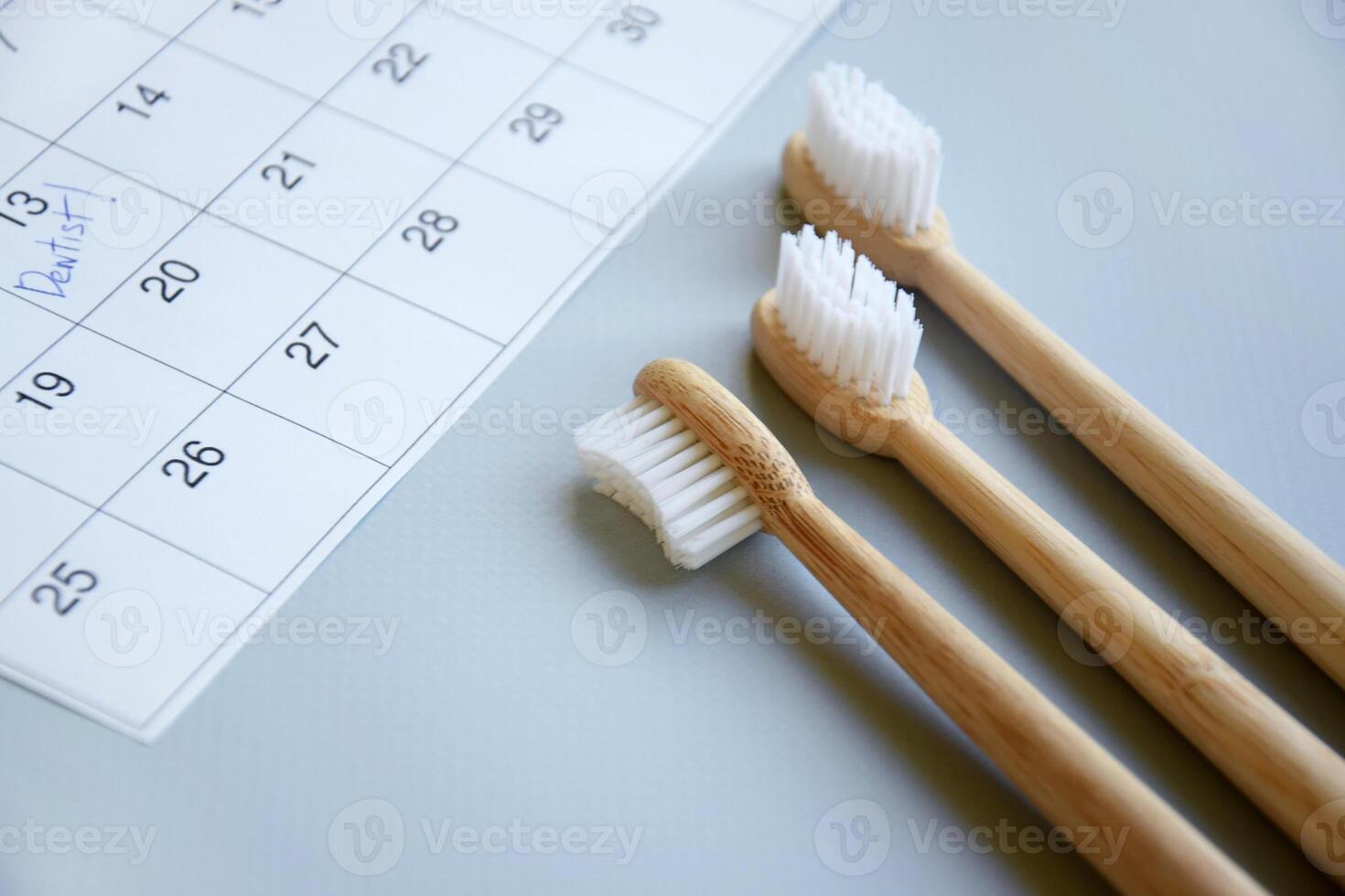 On a light gray background, there is a calendar with a dentist's note and toothbrushes. photo