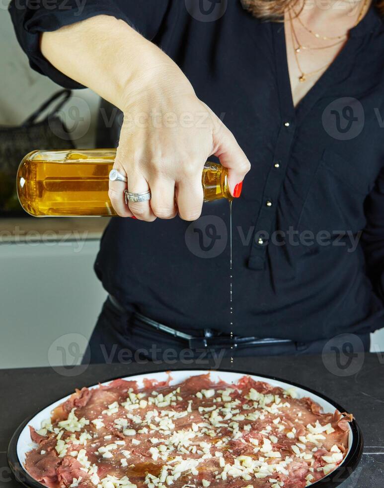 Hostess making carpaccio on marble kitchen countertop with her hands photo