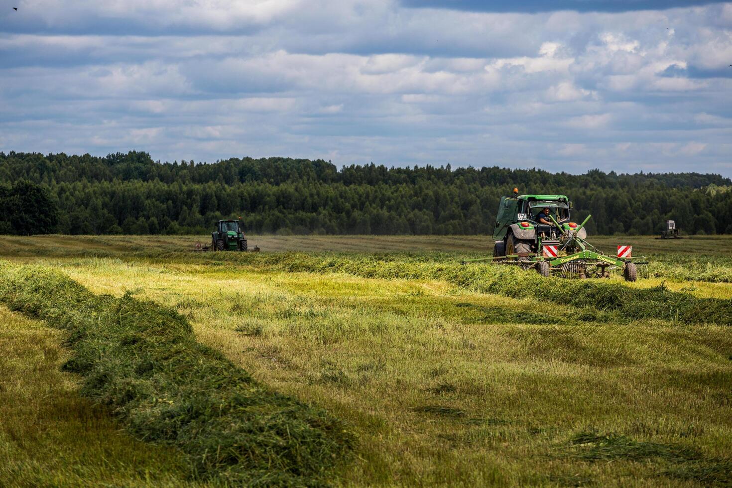 TULA, RUSSIA - JULY 30, 2019 green haymaking tractor on summer field before storm - telephoto shot with selective focus photo
