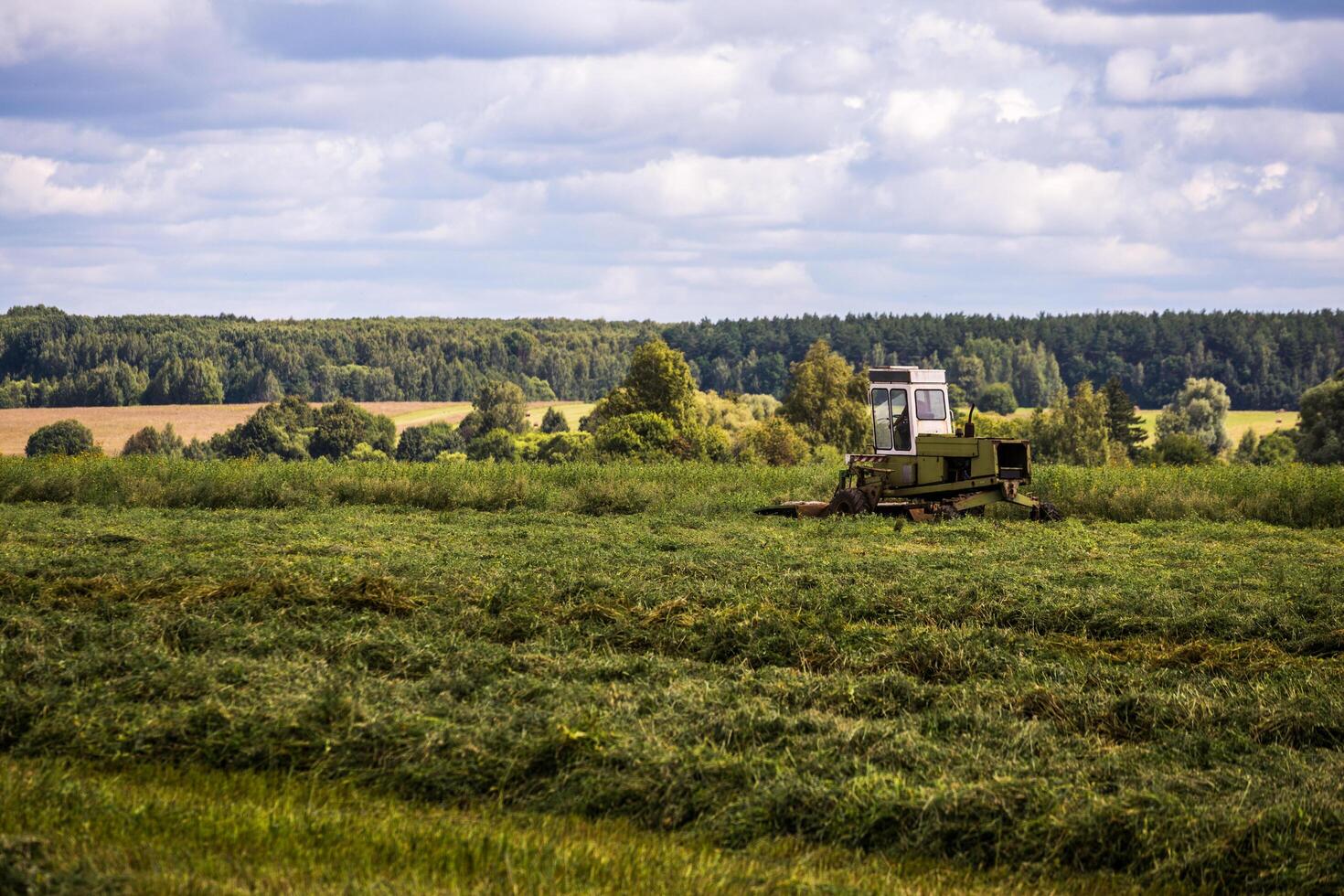 TULA, RUSSIA - JULY 30, 2019 green haymaking tractor on summer field before storm - telephoto shot with selective focus photo