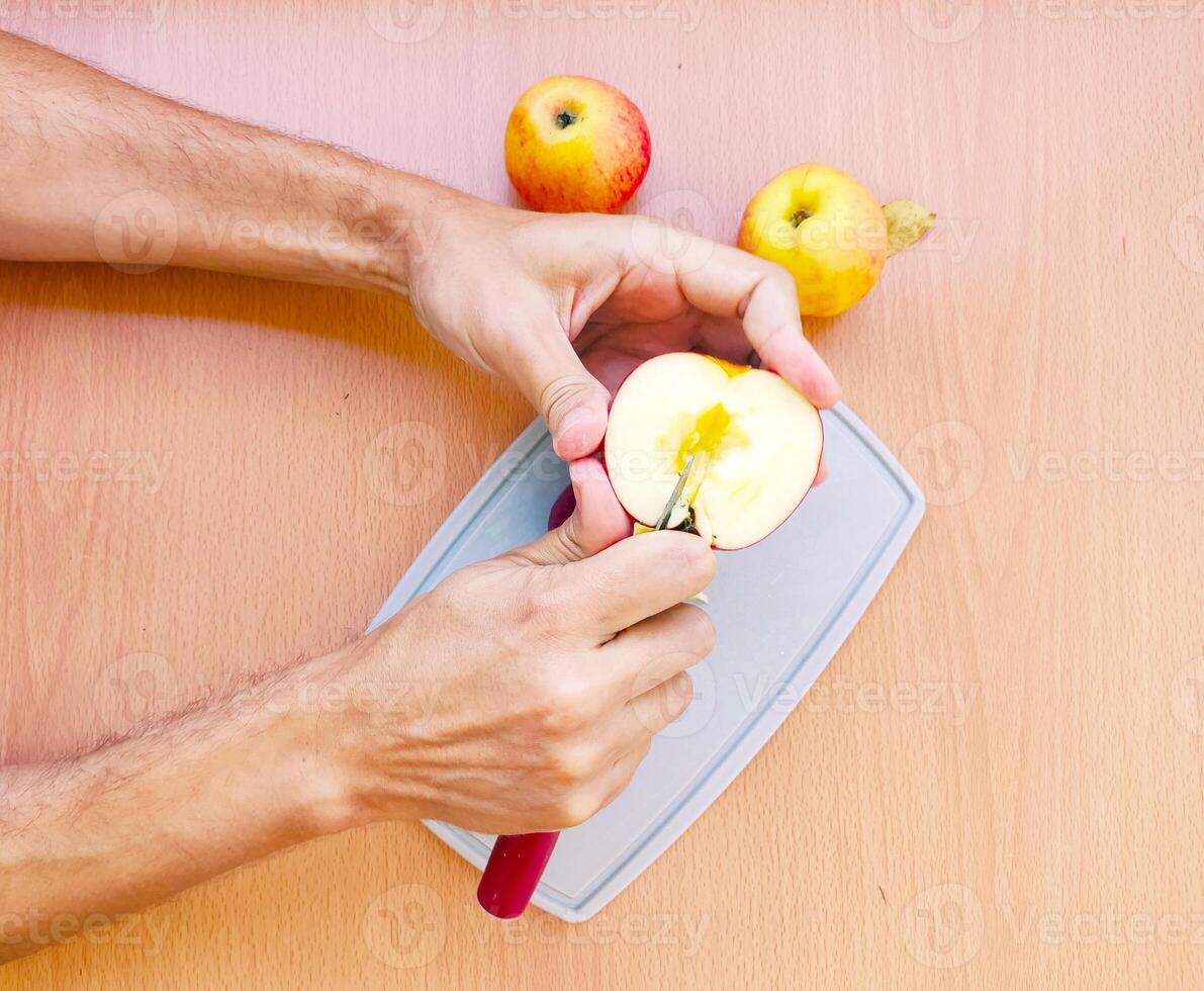 Close up male hands cut an apple into slices. Top view of preparing fruits over kitchen table. photo